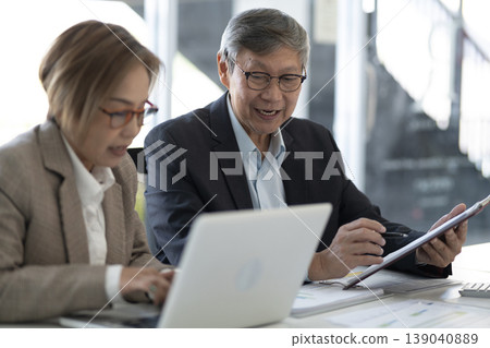 Asian business professionals discuss project collaborate office setting sharing ideas using laptop tablet for corporate strategy financial data analysis Asian business professionals discuss project collaborate office setting sharing ideas using laptop tablet for corporate strategy financial data analysis 139040889