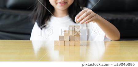 Wooden blocks and cubes form rising step shapes on a table in front of a child, combining gradual learning progress with playful problem solving and early thinking development. 139040896