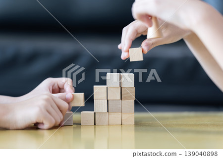 Wooden blocks and cubes form rising step shapes on a table in front of a child, combining gradual learning progress with playful problem solving and early thinking development. Wooden blocks and cubes form rising step shapes on a table in front of a child, combining gradual learning progress with playful problem solving and early thinking development. 139040898