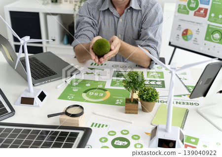 Adult man hands holding moss sphere reviewing ESG environmental sustainability green energy business reports planning renewable power solutions modern office desktop 139040922