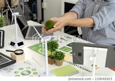 Adult hands nurturing moss ball alongside green energy models office desk promoting sustainable business practices environmental solutions Adult hands nurturing moss ball alongside green energy models office desk promoting sustainable business practices environmental solutions 139040923