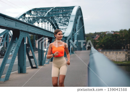 Beautiful young woman running in the morning. Fitness girl listening to music through wireless earphones outdoors Beautiful young woman running in the morning. Fitness girl listening to music through wireless earphones outdoors 139041588