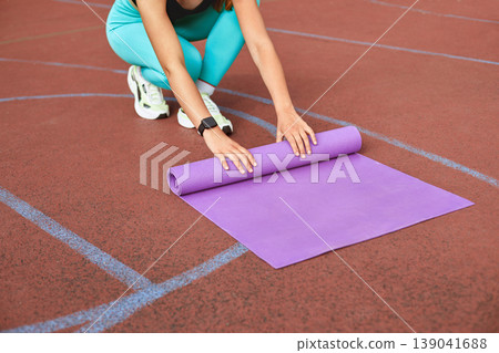 Woman Unrolling a Yoga Mat on a Track Surface for Exercise During a Sunny Day 139041688