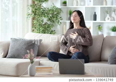 Asian woman doing online guided breathing exercises Asian woman doing online guided breathing exercises 139041749