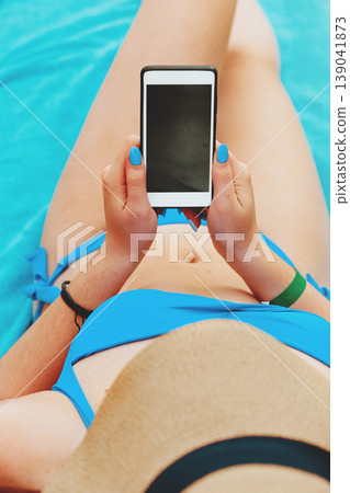 Young attractive woman on a beach by the sea, holding and using a smartphone to take pictures of the scenery. People travel technology outdoors. 139041873