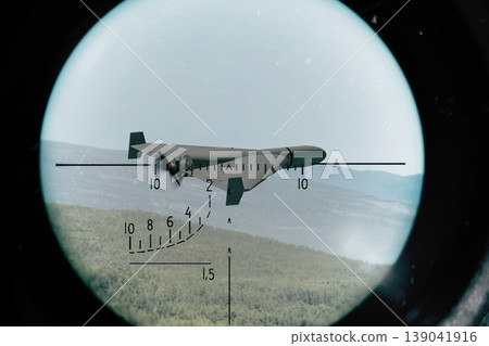 A military drone flies over green hills and is tracked in an optical surveillance scope. A military drone flies over green hills and is tracked in an optical surveillance scope. 139041916