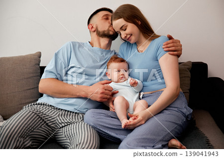Parents share a moment with their baby while sitting on a couch in a living room during the afternoon at home Parents share a moment with their baby while sitting on a couch in a living room during the afternoon at home 139041943