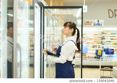 A female store clerk checks the refrigerator inventory. A female store clerk checks the refrigerator inventory. 139042046