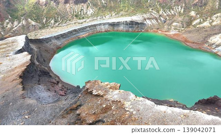 Rugged rock faces and a vibrant emerald green crater lake 139042071