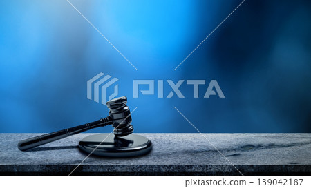 A black judge's gavel rests on a stone surface against a blurred blue background, symbolizing law, justice, and legal authority A black judge's gavel rests on a stone surface against a blurred blue background, symbolizing law, justice, and legal authority 139042187