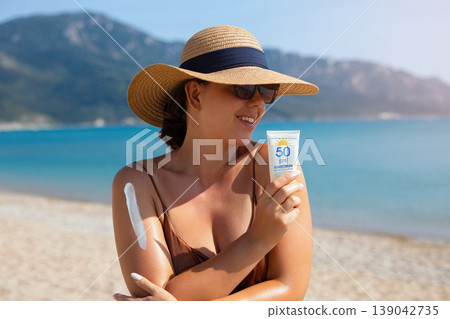 Attractive Woman Holding Sunscreen Bottle And Touching Shoulder At Beach. Beauty Skincare Routine. Female Protecting Skin From Sun Exposure Attractive Woman Holding Sunscreen Bottle And Touching Shoulder At Beach. Beauty Skincare Routine. Female Protecting Skin From Sun Exposure 139042735