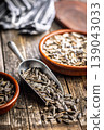 Sunflower Seeds in Metal Scoop on Rustic Wooden Table With Ceramic Bowls for Snacking and Cooking 139043033