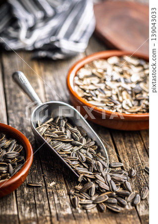 Sunflower Seeds in Metal Scoop on Rustic Wooden Table With Ceramic Bowls for Snacking and Cooking 139043033