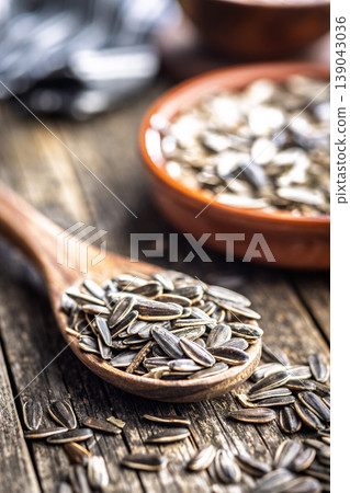 Close-Up of Sunflower Seeds in Wooden Spoon With Rustic Bowl on Weathered Table 139043036