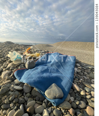 Blanket and stones on rocky beach with cloudy sky and distant boat near shoreline Blanket and stones on rocky beach with cloudy sky and distant boat near shoreline 139043084