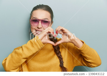 Young woman making heart shape with hands smiling in yellow sweater on blue background expressing love positivity and lifestyle beauty portrait Young woman making heart shape with hands smiling in yellow sweater on blue background expressing love positivity and lifestyle beauty portrait 139043112
