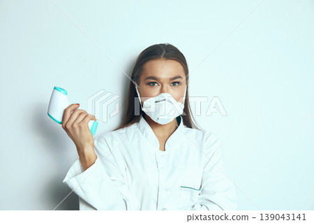 Medical professional wearing a mask holds a device in a studio setting during daytime for health checks and monitoring patient conditions 139043141