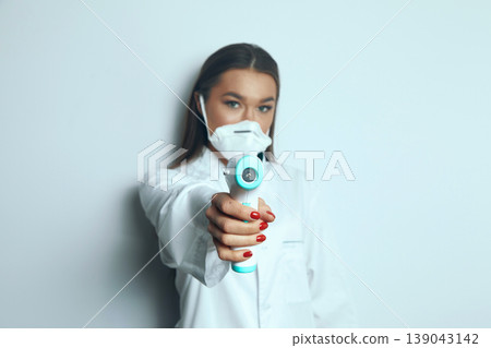 Health professional holds a thermometer while wearing a mask and headset in a clean room during a health check Health professional holds a thermometer while wearing a mask and headset in a clean room during a health check 139043142