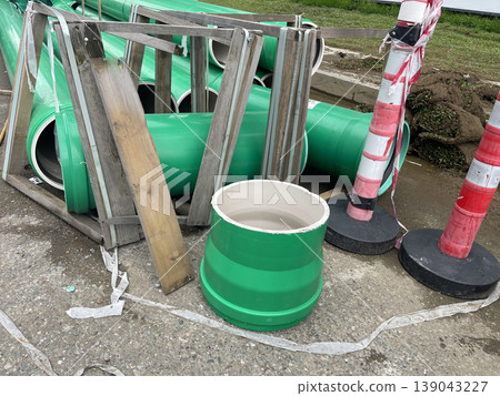Construction site shows green pipes, wooden frames, and traffic cones in a work area during day time 139043227