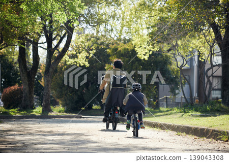 A child and their father riding bicycles in a park in spring. 139043308