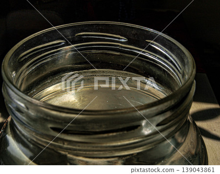 Macro shot of a large glass jar neck with a rhythmic thread pattern. Minimalist composition featuring optical refraction, transparent textures and sculptural form in a clear light. Macro shot of a large glass jar neck with a rhythmic thread pattern. Minimalist composition featuring optical refraction, transparent textures and sculptural form in a clear light. 139043861