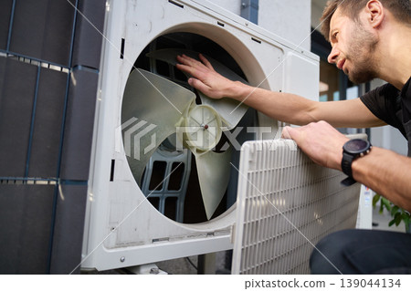 Technician inspecting fan inside outdoor heat pump unit Technician inspecting fan inside outdoor heat pump unit 139044134