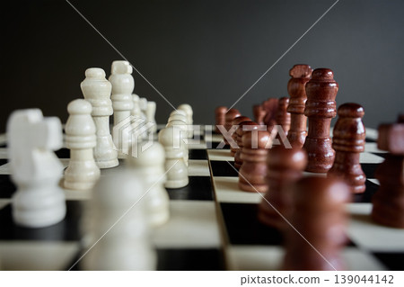 White and brown chess pieces facing each other on chessboard White and brown chess pieces facing each other on chessboard 139044142