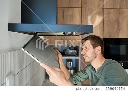 Man removing filter from kitchen range hood for cleaning Man removing filter from kitchen range hood for cleaning 139044154
