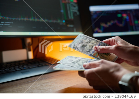 Hands counting dollar bills near monitors with stock market charts 139044169