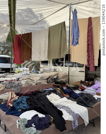 Outdoor market with various textiles hanging and displayed, with clothes spread on tables 139044216
