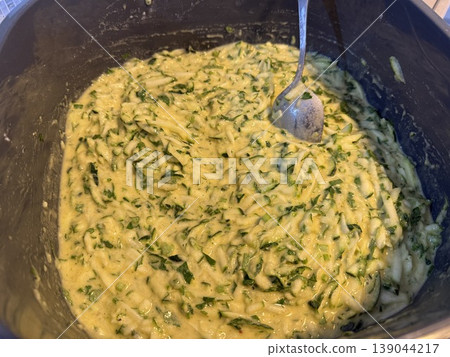 Zucchini batter mixture in a bowl with a spoon, preparing for cooking or baking use Zucchini batter mixture in a bowl with a spoon, preparing for cooking or baking use 139044217