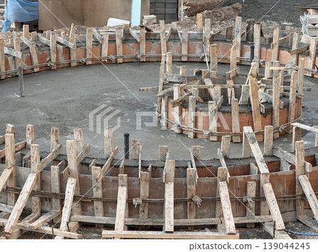Construction site showing circular concrete foundation forms with wooden supports Construction site showing circular concrete foundation forms with wooden supports 139044245