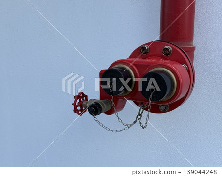 Red fire hydrant connection against plain white wall background, with emergency safety concept Red fire hydrant connection against plain white wall background, with emergency safety concept 139044248