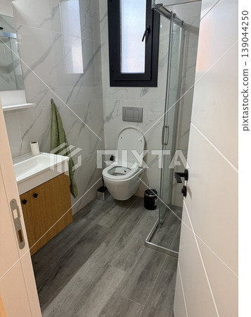Modern bathroom showing toilet, shower, and sink with white and wood materials in small space Modern bathroom showing toilet, shower, and sink with white and wood materials in small space 139044250