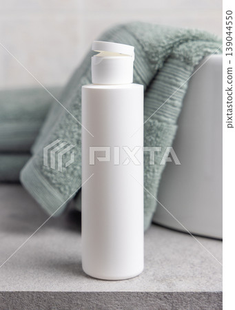 White flip top cosmetic bottle mockup near sage green bath towel in bathroom. Unbranded packaging 139044550