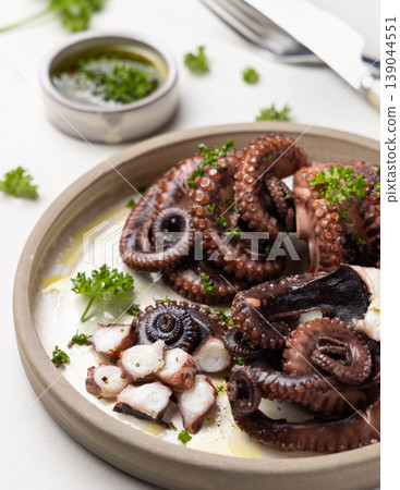 Boiled octopus on ceramic plate with olive oil and parsley dressing. Mediterranean cold appetizer Boiled octopus on ceramic plate with olive oil and parsley dressing. Mediterranean cold appetizer 139044551