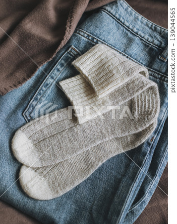 Cosy hand knitted socks with a pair of blue jeans on a brown blanket. 139044565