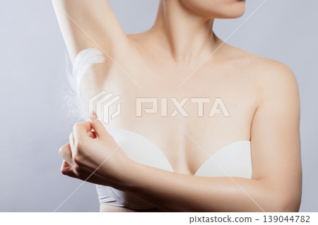 Woman applying lotion to underarm area while wearing a white top in a bright indoor setting Woman applying lotion to underarm area while wearing a white top in a bright indoor setting 139044782