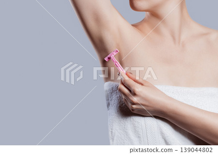 Woman gently shaving armpit epilation hair removal with ergonomic pink shaver. Body care skin care beauty concept Woman gently shaving armpit epilation hair removal with ergonomic pink shaver. Body care skin care beauty concept 139044802