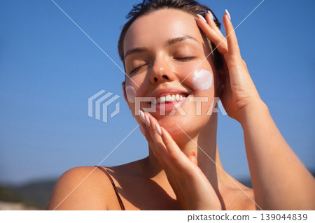 Beautiful Woman Smiling And Touching Face With Sunscreen At Beach. Beauty Skincare Concept. Female Using Sun Cream Beautiful Woman Smiling And Touching Face With Sunscreen At Beach. Beauty Skincare Concept. Female Using Sun Cream 139044839