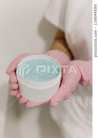 Facial clay mask in white jar in a hands of a cosmetologist. Skin care beauty product. Cosmetology concept. Facial clay mask in white jar in a hands of a cosmetologist. Skin care beauty product. Cosmetology concept. 139044899