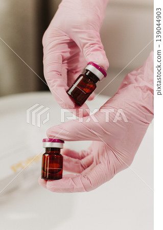 A cosmetologist in rubber pink gloves holding ampoules with a cosmetic product at cosmetology clinic. Close up. Cosmetology concept. 139044903