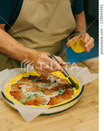 Cooking a traditional Italian pie with cheese and ham on a table in a kitchen. Close up. Cooking a traditional Italian pie with cheese and ham on a table in a kitchen. Close up. 139044992