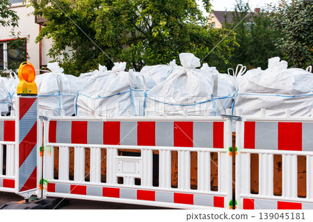 Urban roadwork area with red and white barriers, with white bulk sacks of materials waste in construction waste container Urban roadwork area with red and white barriers, with white bulk sacks of materials waste in construction waste container 139045181