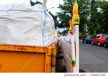 Close up with perspective view of roadwork barriers and construction waste container with sacks on street. Selective focus 139045190