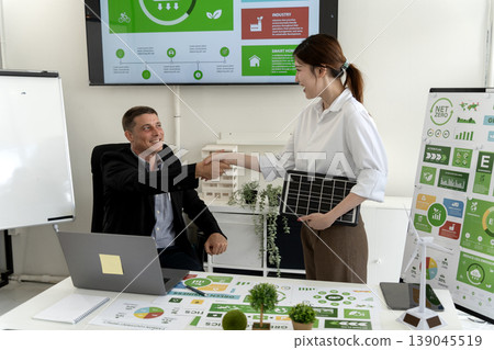 Caucasian man Asian woman shaking hands discussing green business renewable energy solutions solar panel technology office meeting room Caucasian man Asian woman shaking hands discussing green business renewable energy solutions solar panel technology office meeting room 139045519