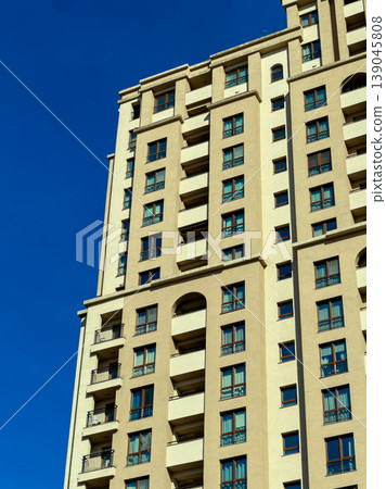 Tall building stands under clear blue sky during daytime with bright sunlight shining on its exterior walls Tall building stands under clear blue sky during daytime with bright sunlight shining on its exterior walls 139045808