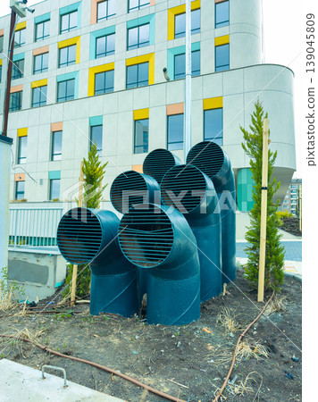 Pipes arranged in a cluster near a modern building with colorful windows in an urban area during daylight Pipes arranged in a cluster near a modern building with colorful windows in an urban area during daylight 139045809