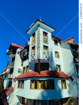 Building with multiple windows and a red roof in a clear blue sky in a town with homes and trees during daytime 139045814