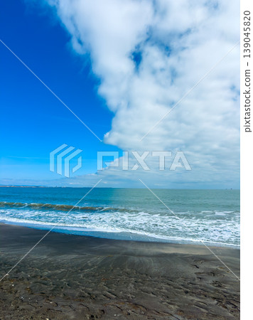 Clouds cover part of the blue sky over the ocean with waves rolling onto a sandy beach on a clear day near the coastline Clouds cover part of the blue sky over the ocean with waves rolling onto a sandy beach on a clear day near the coastline 139045820